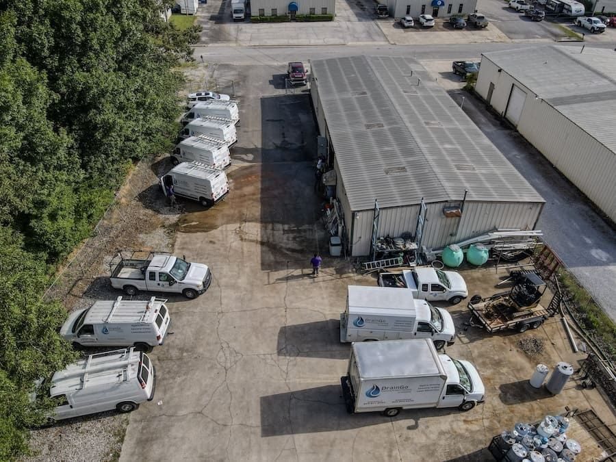 Aerial view of an industrial yard with white service vans, a large metal warehouse, and scattered equipment.