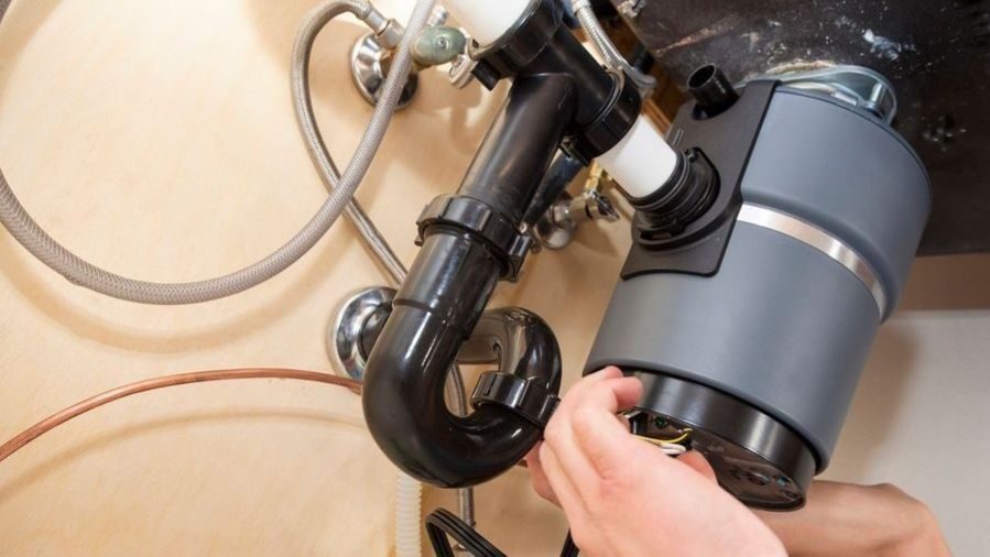 Plumber repairing garbage disposal system under sink.