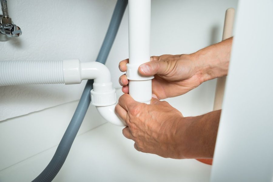 hands unscrewing drain pipe in bathroom