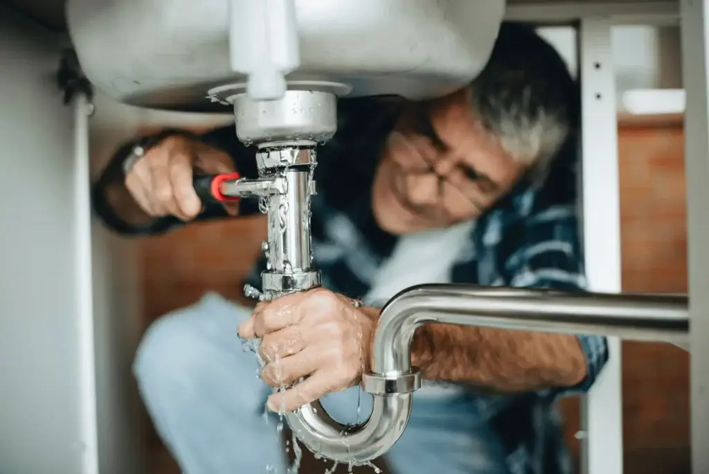 Plumber repairing leaking sink drain pipe under kitchen sink