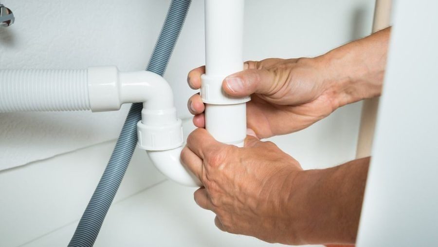 hands unscrewing drain pipe in bathroom
