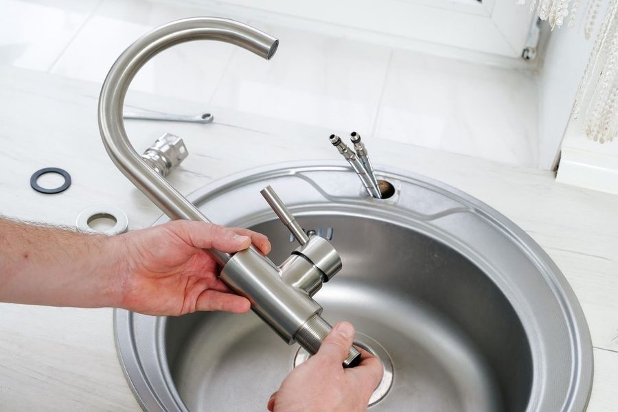 Person tightening a stainless steel kitchen faucet into a round sink basin with their hands.