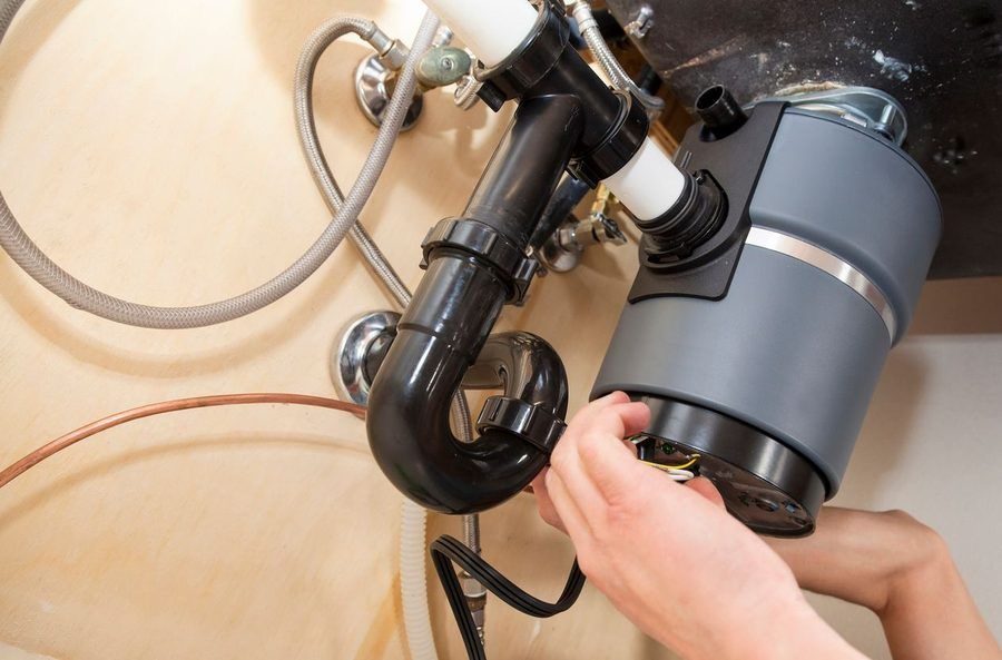 someone fixing a garbage disposal under a kitchen sink