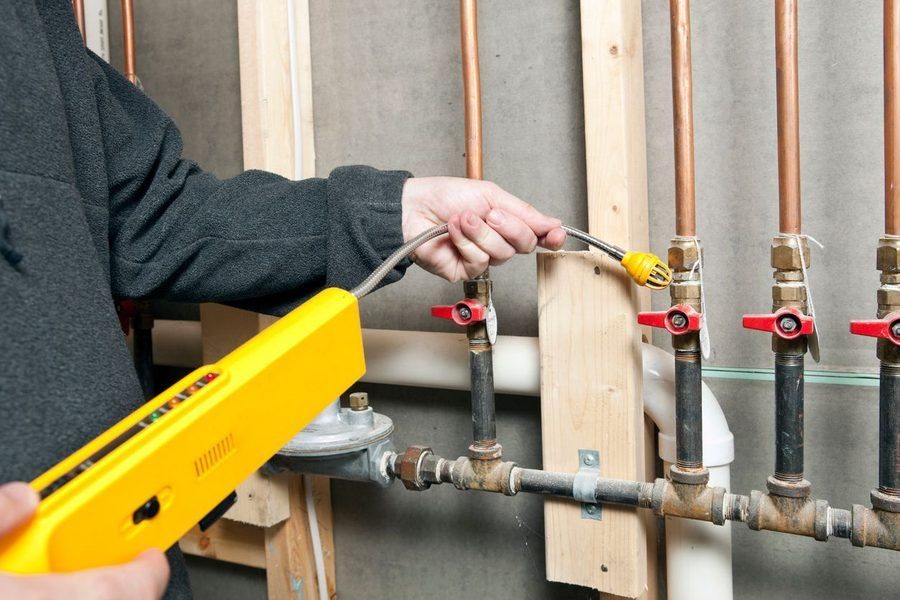 Person using a yellow handheld tester on a copper plumbing line with red shut-off valves under construction framing