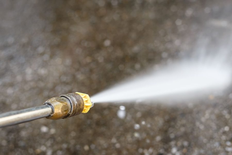 Close-up of a hose nozzle spraying a thin jet of water onto a wet concrete surface.