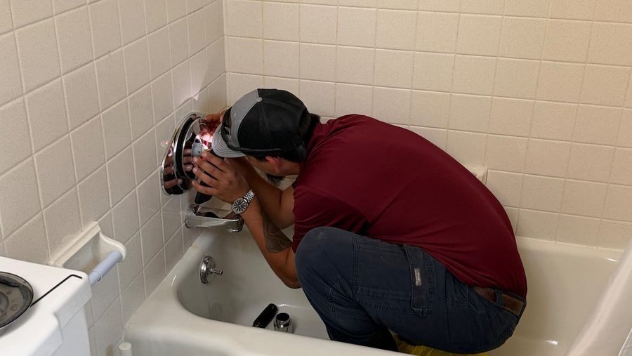 Plumber in bathub repairing or installing shower fixture.