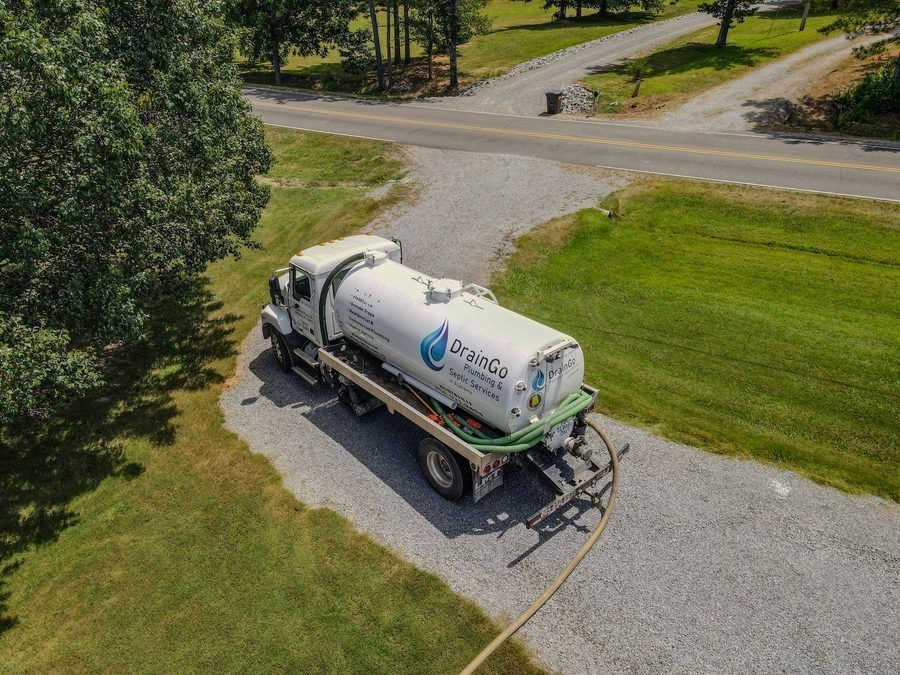 White septic service truck with DrainGo logo parked on a gravel driveway beside a green lawn, connected to a hose for pumping.