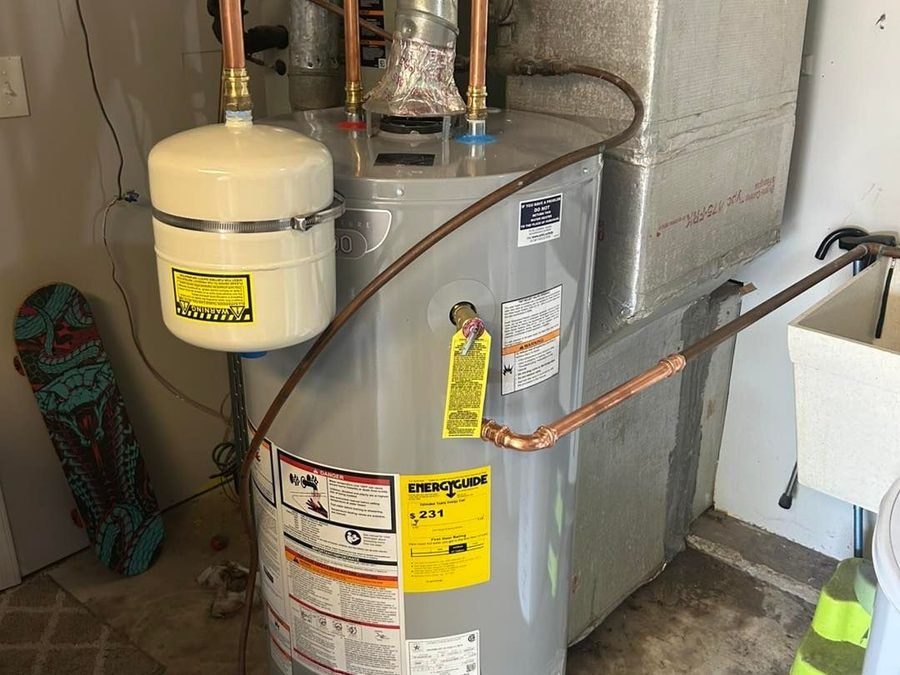 Residential water heater with an expansion tank and copper supply lines in a utility space, showing energy-guide label on the tank
