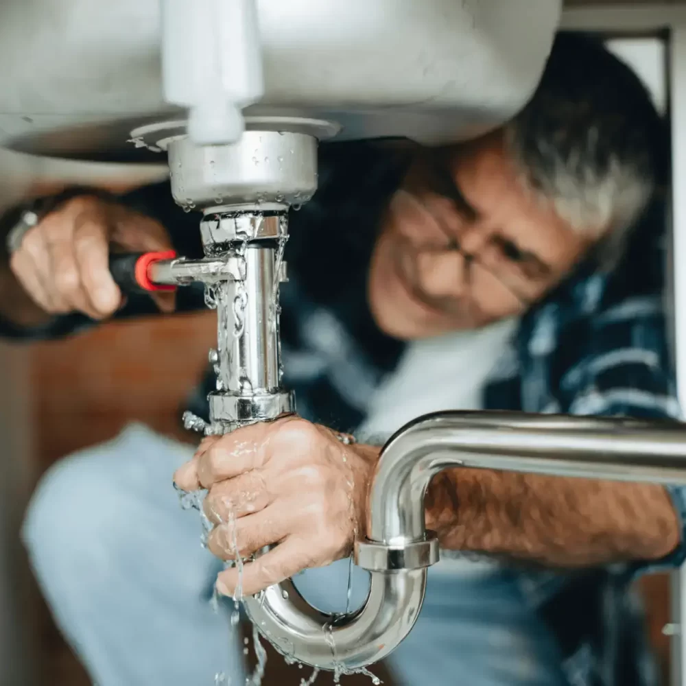 Plumber repairing leaking sink drain pipe under kitchen sink